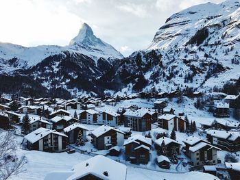 Snow covered houses in town against mountain in winter