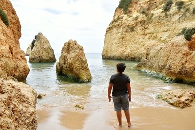 Rear view of woman standing on rock by sea