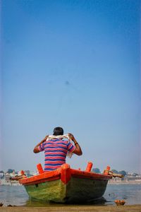 Rear view of man on boat in sea against clear sky