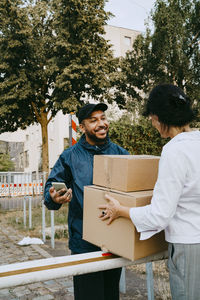 Smiling male delivery person talking with woman while delivering parcels