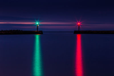 Illuminated lights reflecting on sea against sky at night