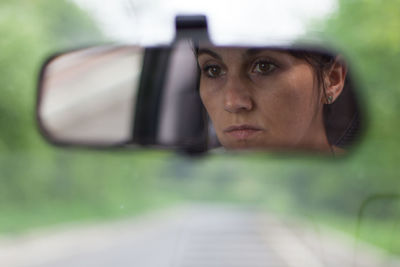 Close-up of mature woman reflecting on rear-view mirror in car