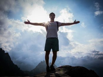 Rear view of silhouette man standing on mountain against cloudy sky