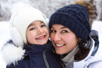 Mom and daughter in warm clothes in the snowy forest hugging and looking into 