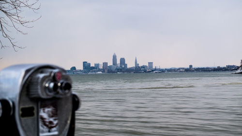 Close-up of camera against cityscape and sea against sky