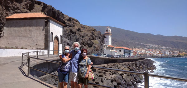 People on sea by buildings against clear sky