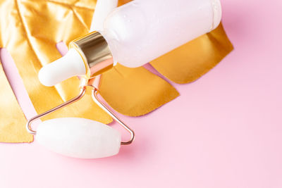 Close up of skin care cosmetic rose oil and quartz face roller for massaging on golden monstera leaf