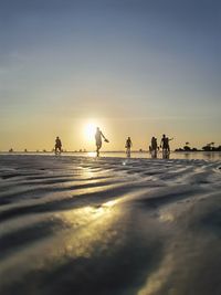 Silhouette people walking at beach against sky during sunset