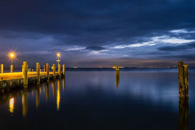 Illuminated wooden posts in lake against sky during sunset
