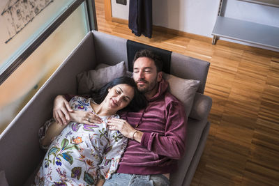 High angle view of couple lying down on sofa at home