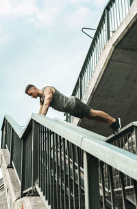 Low angle view of man standing by railing against sky