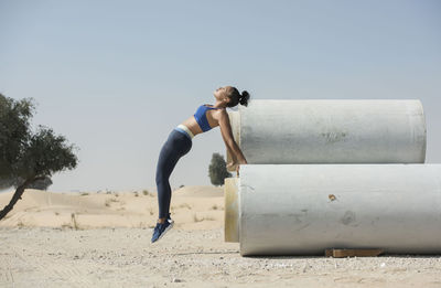 Woman jumping over pipe against sky