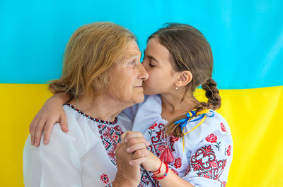Girl kissing grandmother in front of ukrainian flag