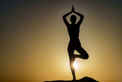 Silhouette woman with arms raised standing against sky during sunset