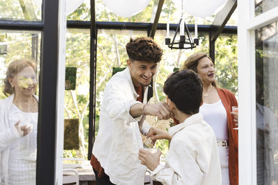 Smiling young man pinching boy's cheek during midsummer party at back yard