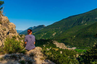 Rear view of man looking at mountains against blue sky