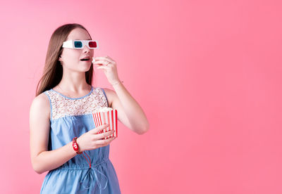 Woman wearing sunglasses standing against pink background