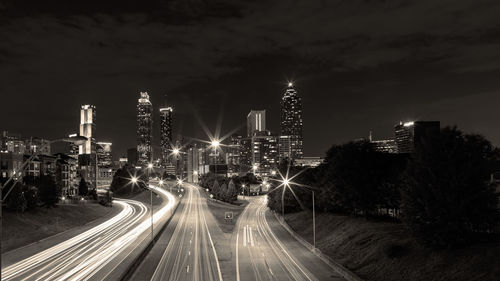 Light trails on road amidst buildings against sky at night