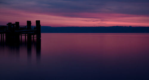 Silhouette pier on lake against cloudy sky during sunset