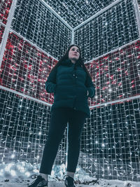 Low angle view of woman standing against metallic fence during winter