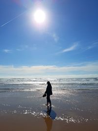 Silhouette woman walking at seashore on sunny day