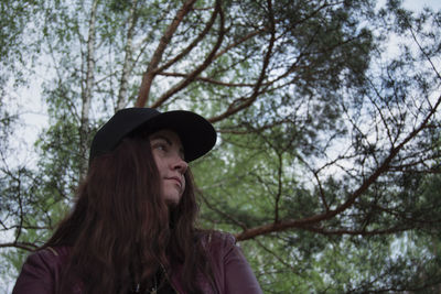 Portrait of young woman looking away against trees