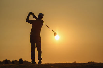 Silhouette man playing golf land against clear sky during sunset