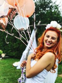 Portrait of smiling young bride holding helium balloons