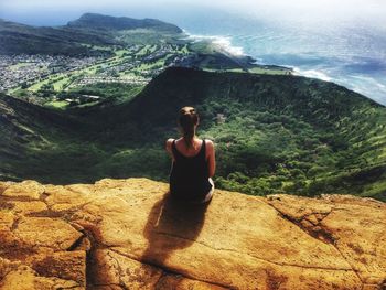 Rear view of woman sitting on rock against sky