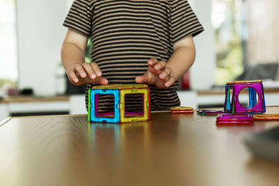 Midsection of boy playing with toy block on table at home