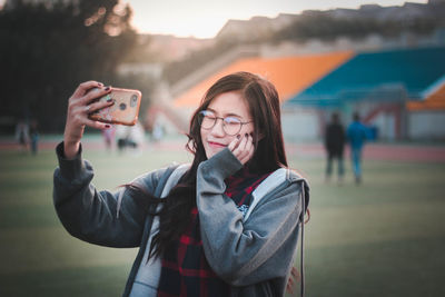 Smiling young woman taking selfie while standing outdoors