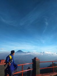 Rear view of man standing on mountain against blue sky