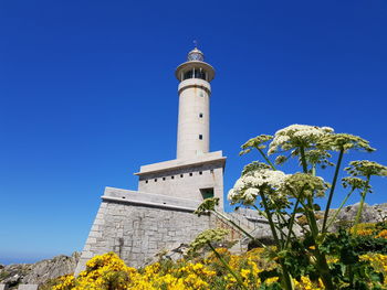 Low angle view of lighthouse by building against clear blue sky