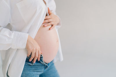 Midsection of pregnant woman with arms crossed standing against wall