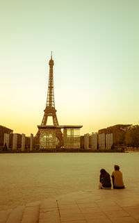 Couple sitting by river against eiffel tower during sunset