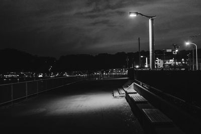 Illuminated street by river against sky at night