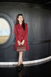 Smiling mature woman holding purse while standing against wall