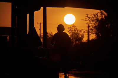 Rear view of silhouette man standing against orange sky