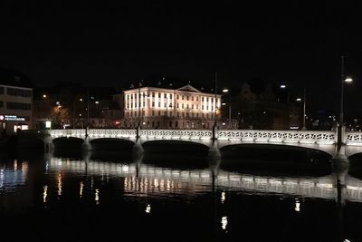 Illuminated bridge over river in city at night
