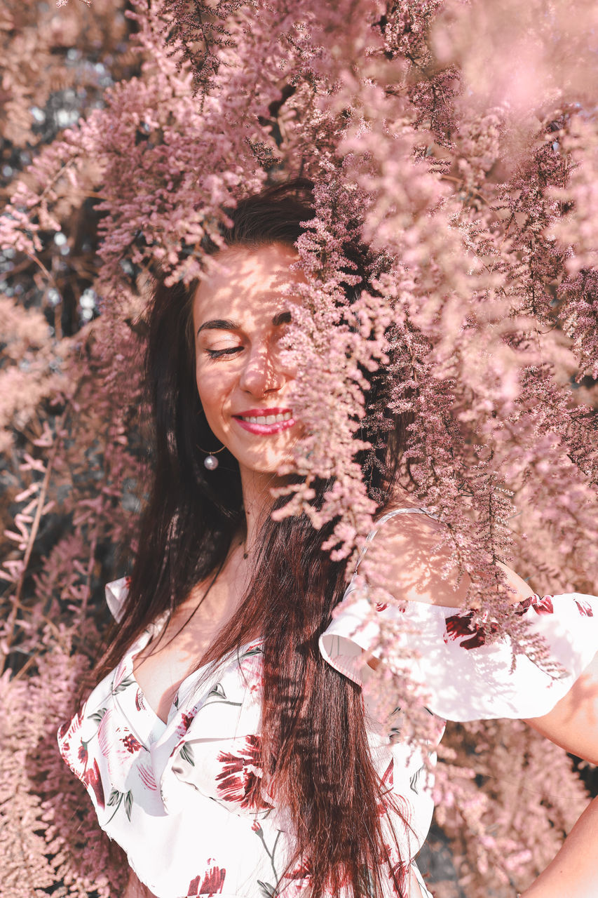 one person, spring, women, adult, young adult, nature, portrait, hairstyle, plant, long hair, pink, flower, brown hair, beauty in nature, smiling, tree, lifestyles, flowering plant, outdoors, happiness, clothing, fashion, land, female, relaxation, eyes closed, emotion, looking, springtime, leisure activity, person, tranquility, sunlight, day, freshness