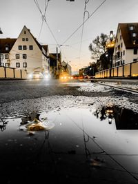 Wet road by illuminated buildings in city during rainy season
