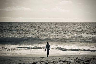 Rear view of man walking at beach against sky