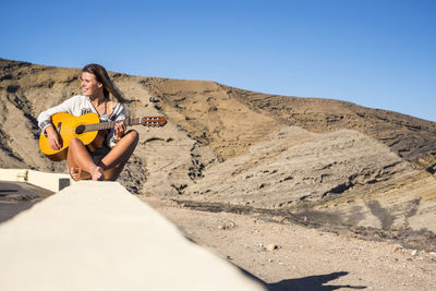 Young woman sitting on land against clear sky