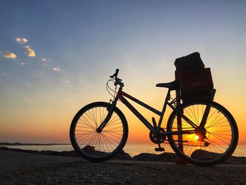 Bicycle at beach against sky during sunset