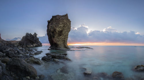 Rock formation on beach against sky during sunset