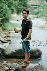 Young man looking away while standing on rock