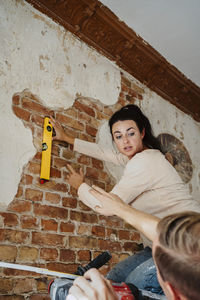 Man assisting woman in measuring brick wall while renovating home