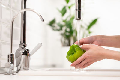 Wash before eat. female washing green pepper in water in sink before cooking salad. hygiene concept
