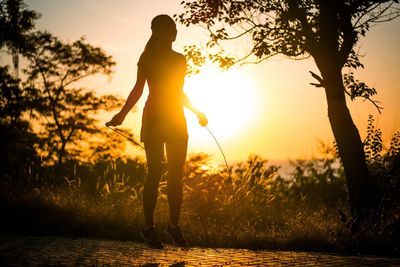 Silhouette woman standing by trees against sky during sunset