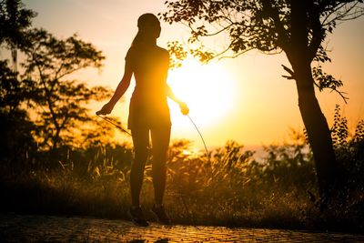 Silhouette woman exercising by trees against sky during sunset